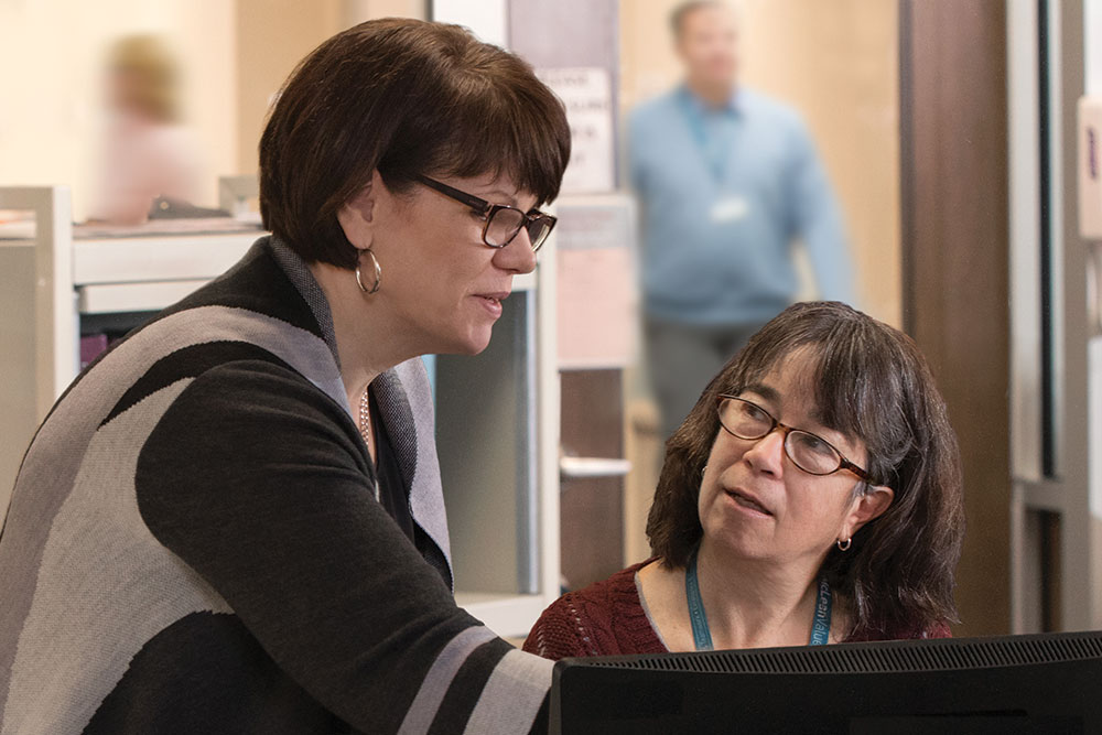 Two women discuss something on computer screen
