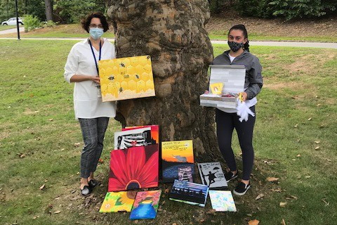 Two women stand by tree with paintings
