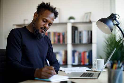 Adult man with a laptop taking notes with a pen and paper