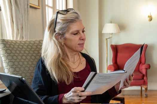 Woman sits reading stapled papers in well-appointed living room