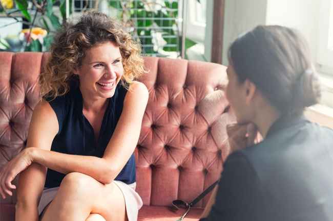 Woman on red couch talks to another woman