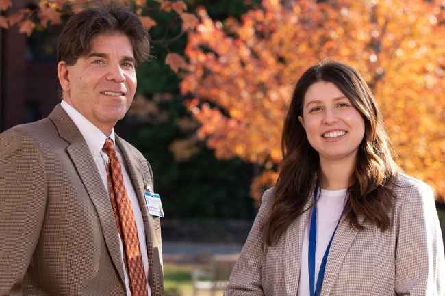 Two faculty members in front of orange leaf tree