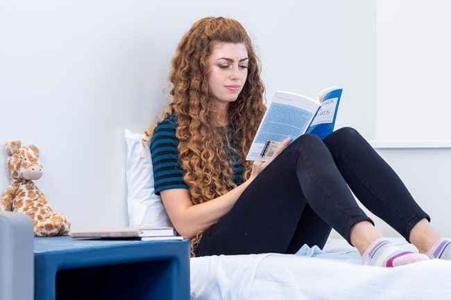 Young woman reads sitting on bed