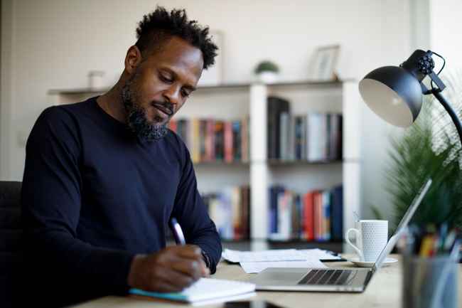 Adult man with a laptop taking notes with a pen and paper
