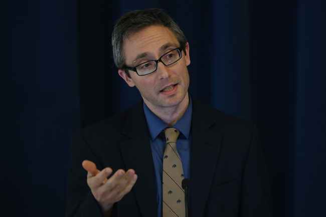 Person with short hair and glasses talking into a microphone
