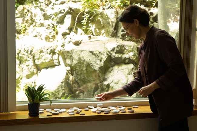 Person with dark hair looking at stones in front of a large window