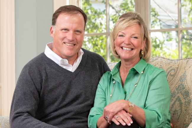 Two people sitting on a couch and smiling in front of a bright window
