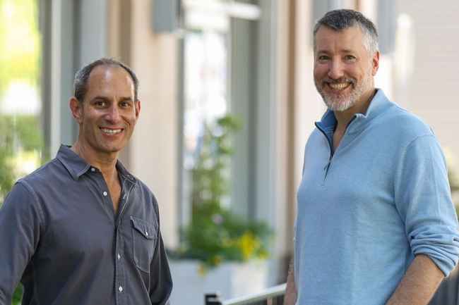 Two men pose outside a building