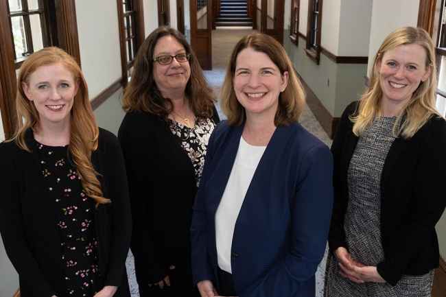 4 women pose in a hallway with windows