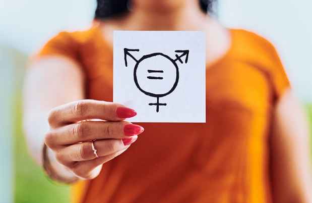 Woman in orange shirt holding a piece od paper with diverse gender symbols on it.