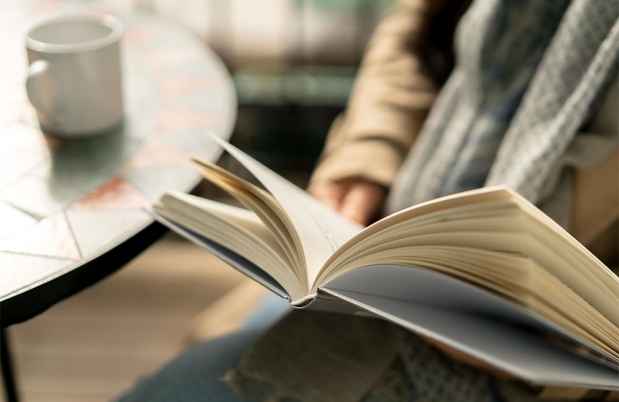 Hand holding book, coffee cup on table