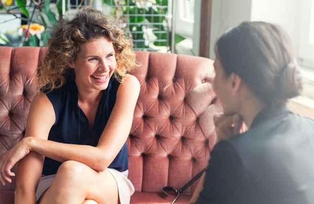 Woman on red couch talks to another woman