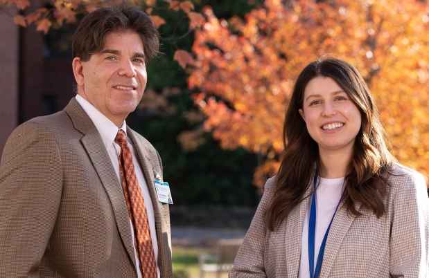 Two faculty members in front of orange leaf tree