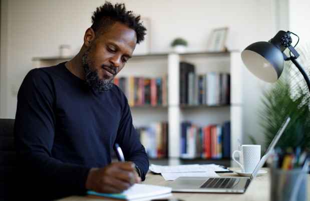 Adult man with a laptop taking notes with a pen and paper