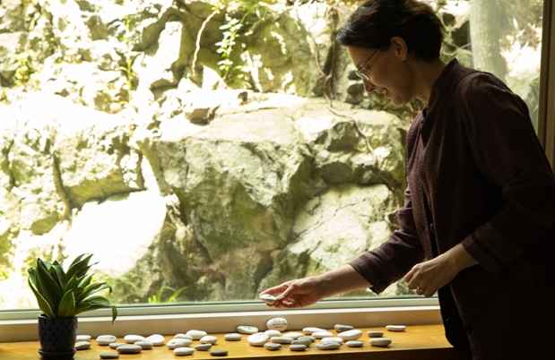 Person with dark hair looking at stones in front of a large window