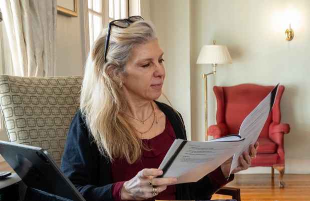 Woman sits reading stapled papers in well-appointed living room