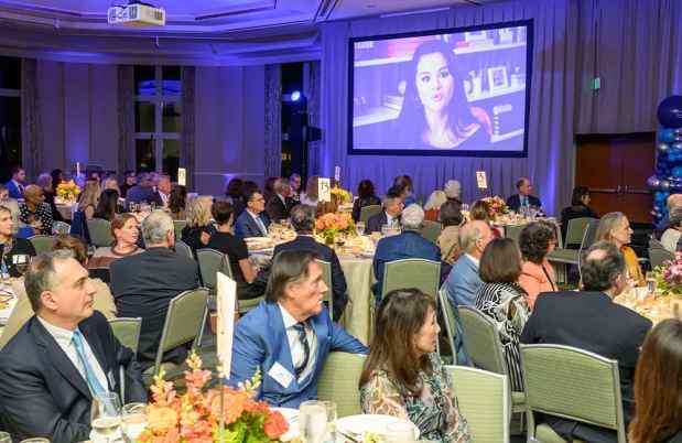 People sitting at tables looking at a screen with a woman talking