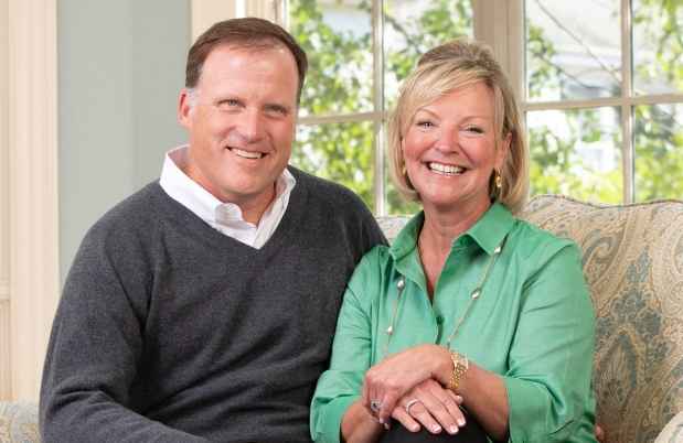 Two people sitting on a couch and smiling in front of a bright window