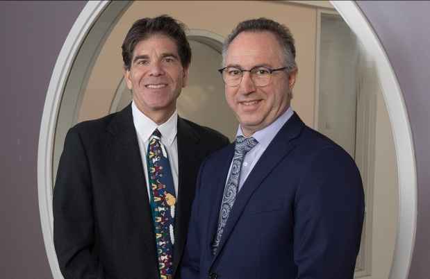 Two people in suits smiling in front of a circular window
