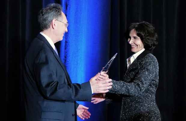 One person hands another person a clear glass award in front of dark blue curtain