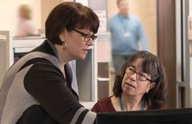 Two nurses discuss something on a computer screen