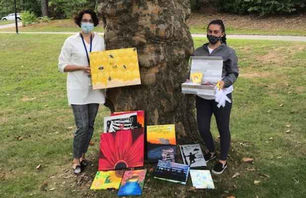 Two women stand by tree with paintings