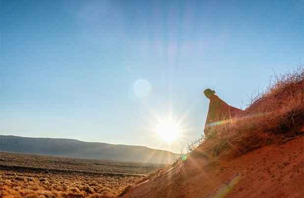 Indigenous person in blanket sitting on side of a hill.