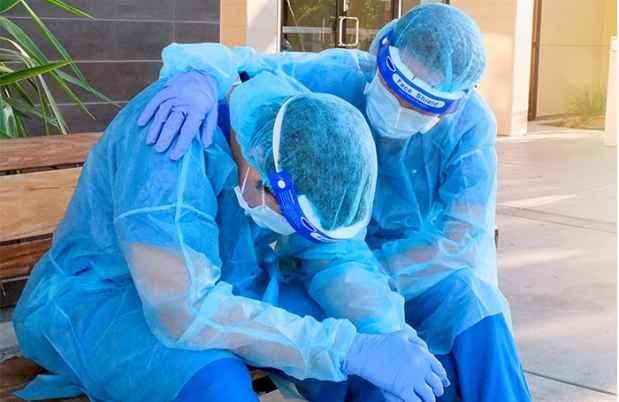 Pandemic frontline worker consoling another who has head down.