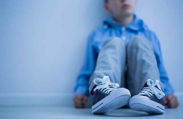 Young boy sitting on the ground with his blue sneakers in the foreground.