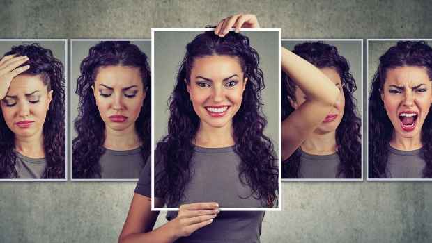 Woman holding up picture with a bunch of different pictures with facial expressions on them. 