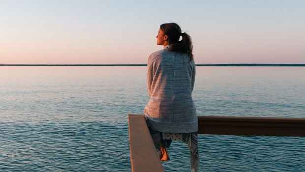 Woman sits on railing by the sea