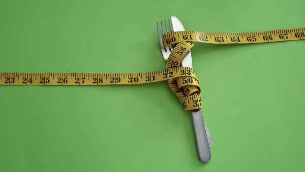 Knife and fork wrapped in measuring tape on green background