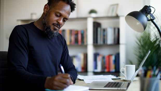 Adult man with a laptop taking notes with a pen and paper