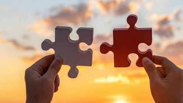 Two hands holding large jigsaw puzzle pieces in front of a sunset